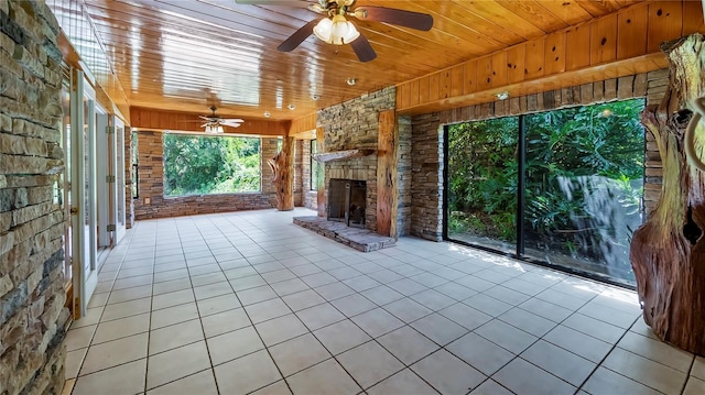 unfurnished living room with light tile patterned floors, brick wall, an outdoor stone fireplace, and wood ceiling