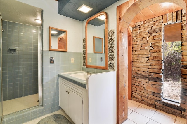 full bath featuring tile patterned flooring, a wainscoted wall, vanity, tile walls, and a shower stall