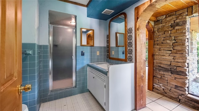 bathroom featuring a stall shower, a wainscoted wall, tile patterned flooring, vanity, and tile walls