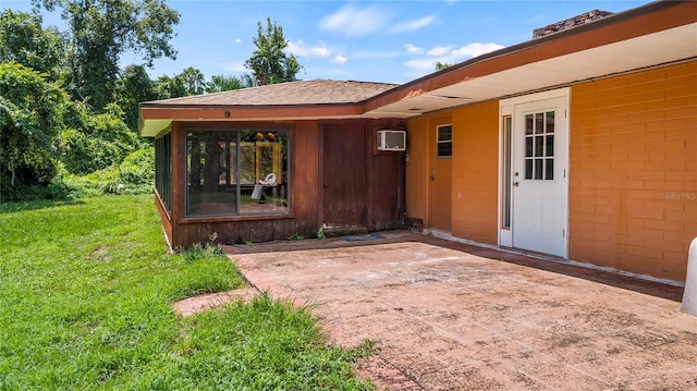 entrance to property featuring a shingled roof, an AC wall unit, a patio area, and a lawn