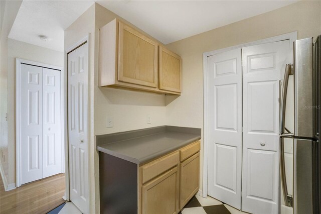 kitchen with light brown cabinetry, light floors, dark countertops, and freestanding refrigerator
