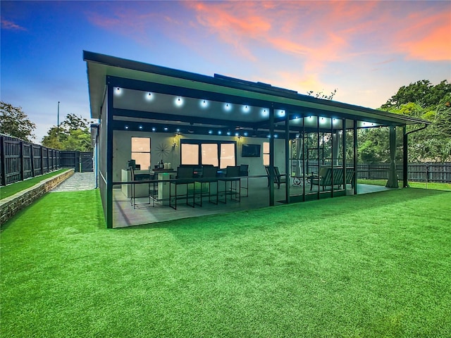 back house at dusk with a patio and a lawn