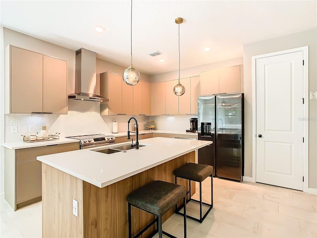 kitchen featuring appliances with stainless steel finishes, a kitchen island with sink, wall chimney range hood, and sink