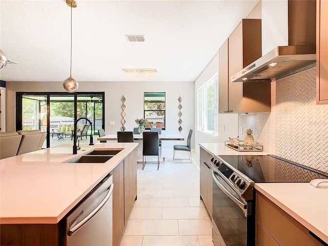 kitchen with sink, stainless steel appliances, wall chimney exhaust hood, and a healthy amount of sunlight