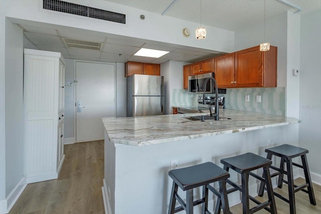 kitchen featuring light wood-type flooring, tasteful backsplash, kitchen peninsula, appliances with stainless steel finishes, and a breakfast bar area