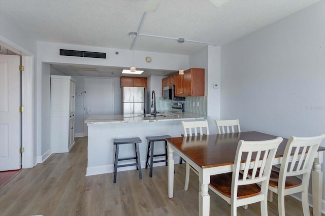 kitchen featuring pendant lighting, light hardwood / wood-style flooring, appliances with stainless steel finishes, backsplash, and kitchen peninsula