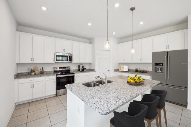 kitchen with an island with sink, appliances with stainless steel finishes, white cabinetry, pendant lighting, and a sink