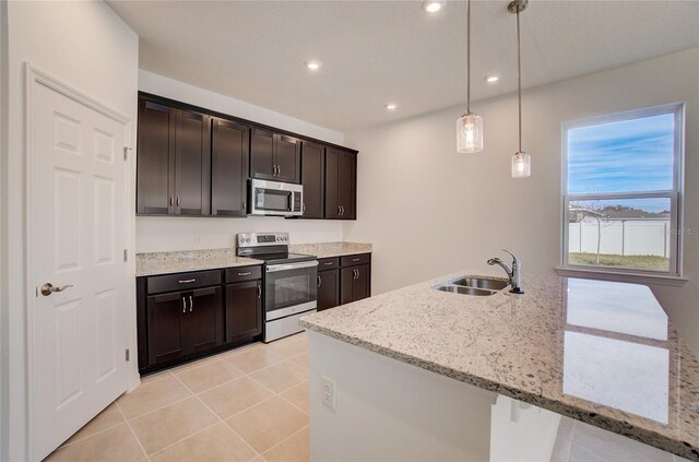 kitchen featuring light stone counters, appliances with stainless steel finishes, hanging light fixtures, dark brown cabinets, and a sink