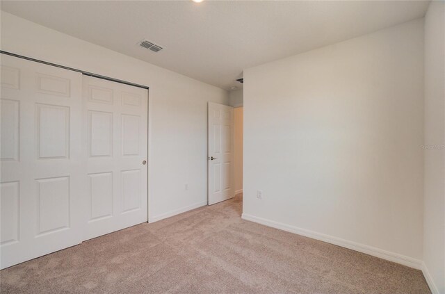 unfurnished bedroom featuring baseboards, visible vents, a closet, and light colored carpet