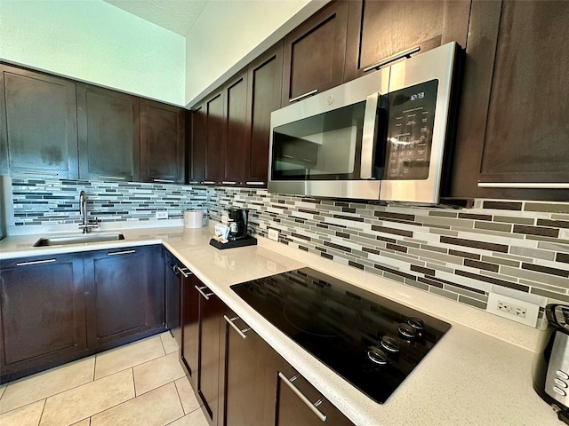 kitchen with black electric stovetop, stainless steel microwave, a sink, and tasteful backsplash