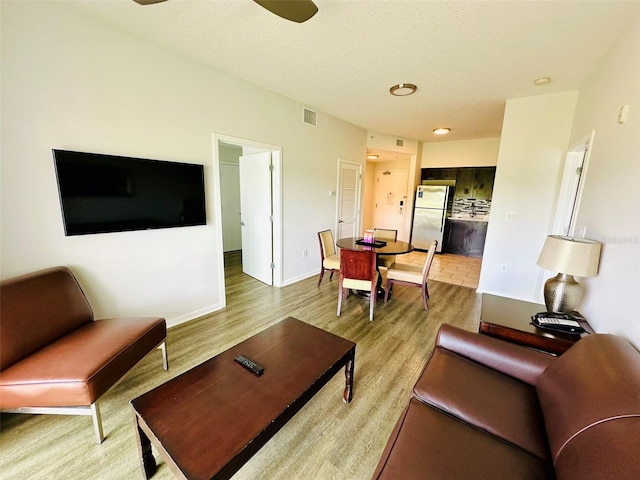 living area featuring visible vents, a textured ceiling, baseboards, and wood finished floors