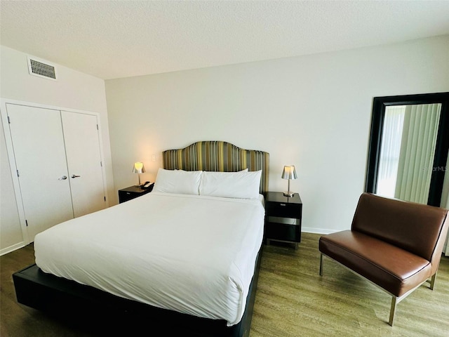 bedroom with a closet, visible vents, a textured ceiling, wood finished floors, and baseboards