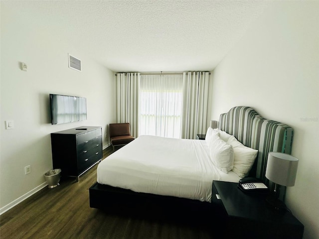 bedroom with a textured ceiling, dark wood-style flooring, visible vents, and baseboards