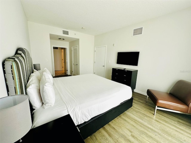 bedroom featuring light wood-style floors, visible vents, a textured ceiling, and baseboards