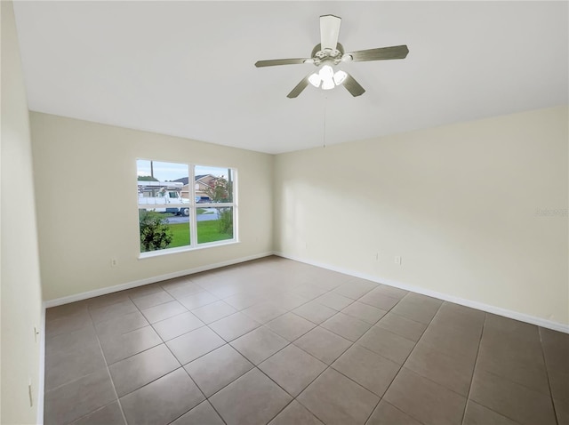 tiled empty room featuring a ceiling fan and baseboards