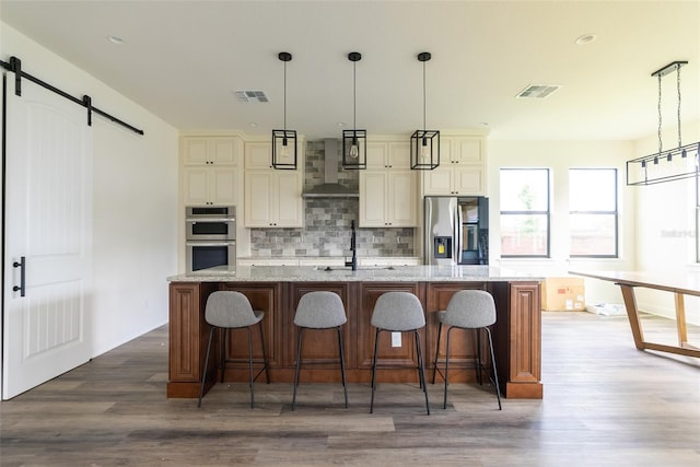 kitchen with wall chimney exhaust hood, light stone counters, dark hardwood / wood-style floors, a barn door, and stainless steel appliances