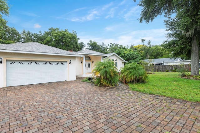 view of front of property featuring a front yard, fence, an attached garage, stucco siding, and decorative driveway