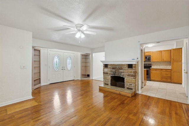 unfurnished living room featuring a fireplace, light wood-type flooring, built in features, and ceiling fan