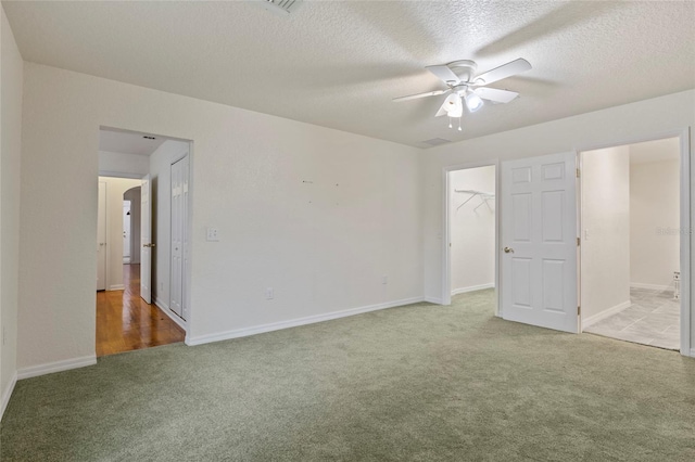 unfurnished bedroom with ceiling fan, a spacious closet, a closet, and light carpet