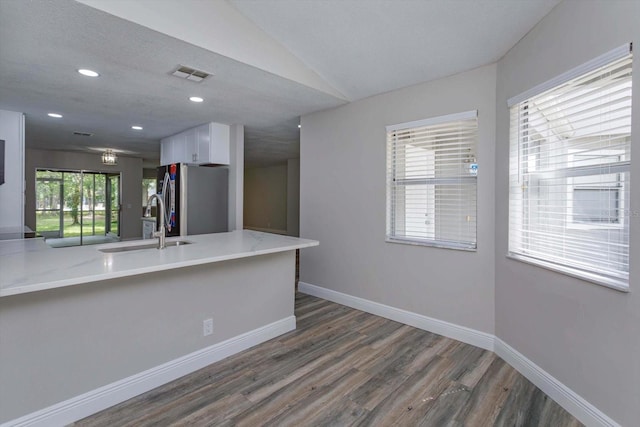 kitchen with white cabinets, vaulted ceiling, dark hardwood / wood-style flooring, stainless steel refrigerator, and sink