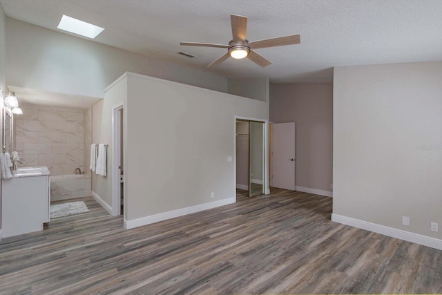 unfurnished living room with vaulted ceiling with skylight, a textured ceiling, sink, ceiling fan, and dark hardwood / wood-style floors