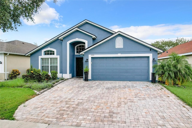 ranch-style home featuring a garage, decorative driveway, and stucco siding