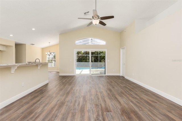 unfurnished living room with high vaulted ceiling, dark wood-type flooring, and ceiling fan with notable chandelier