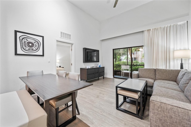 living room with visible vents, a high ceiling, ceiling fan, and light wood finished floors