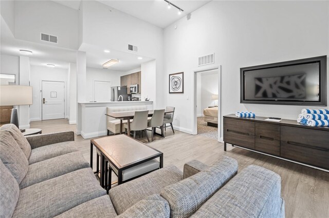 living room featuring a towering ceiling, light wood-type flooring, and rail lighting