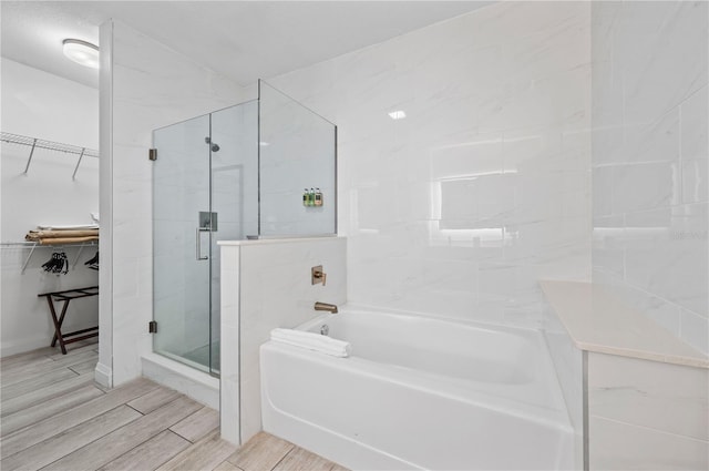 full bath with a spacious closet, a shower stall, a bath, and wood tiled floor