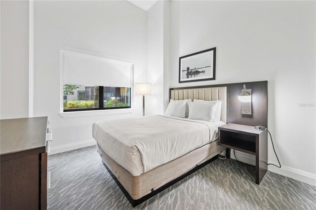 bedroom with dark carpet and a towering ceiling