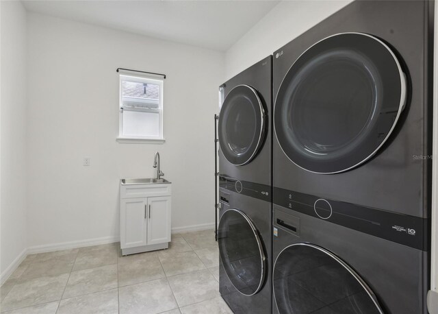 clothes washing area featuring cabinets, sink, light tile patterned floors, and stacked washing maching and dryer