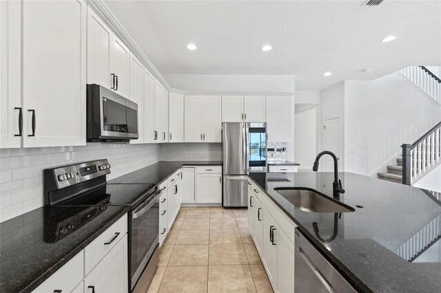 kitchen featuring appliances with stainless steel finishes, white cabinetry, backsplash, dark stone counters, and sink