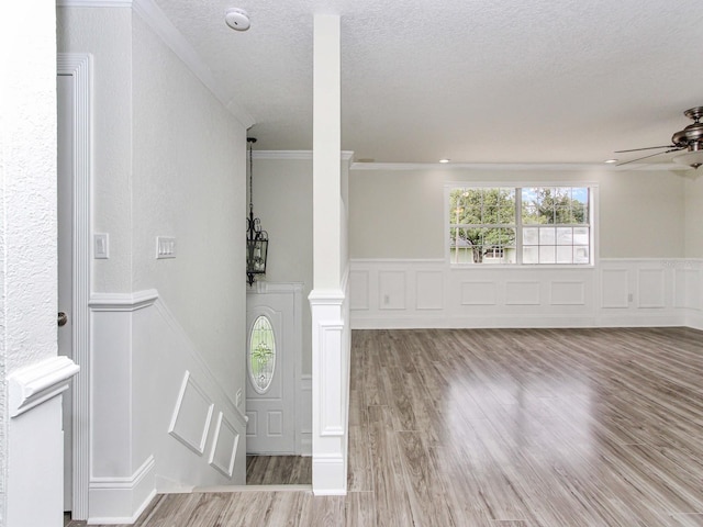 entryway featuring ornamental molding, a textured ceiling, wood finished floors, a decorative wall, and ceiling fan