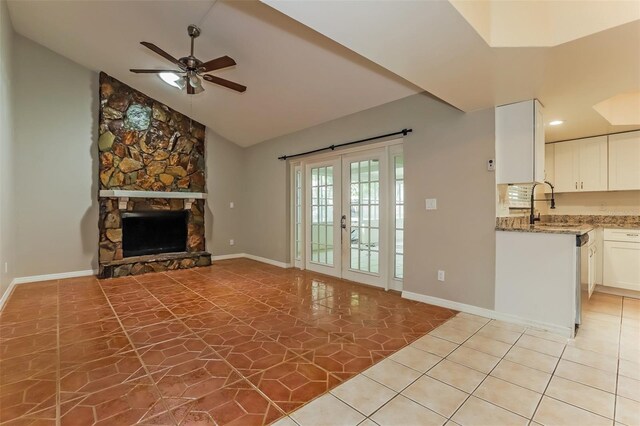 unfurnished living room with vaulted ceiling, french doors, a fireplace, light tile patterned floors, and ceiling fan