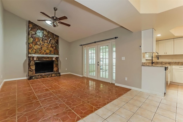 unfurnished living room with a ceiling fan, french doors, lofted ceiling, a stone fireplace, and a sink