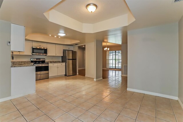 kitchen featuring a tray ceiling, dark stone countertops, an inviting chandelier, light tile patterned flooring, and stainless steel appliances