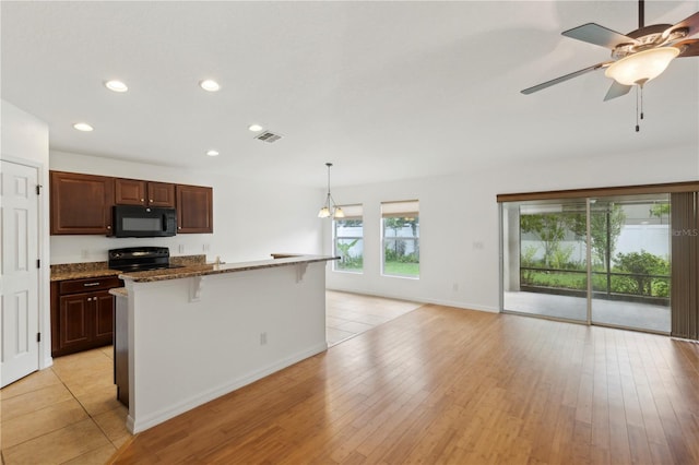 kitchen featuring a kitchen island with sink, black appliances, hanging light fixtures, dark stone countertops, and a kitchen bar