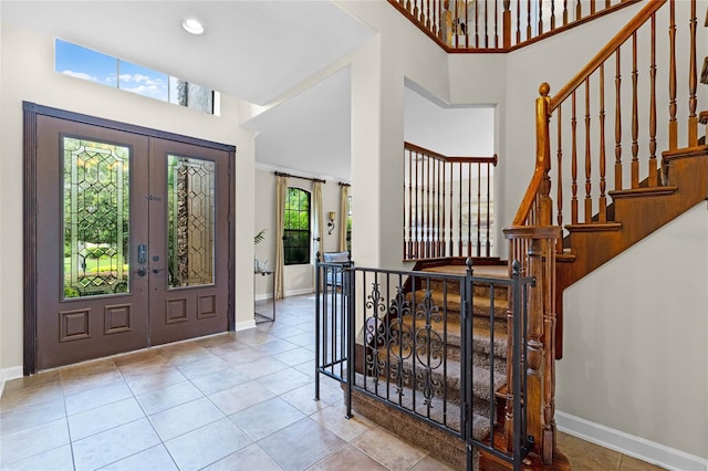 foyer with a wealth of natural light, a towering ceiling, french doors, and light tile patterned flooring