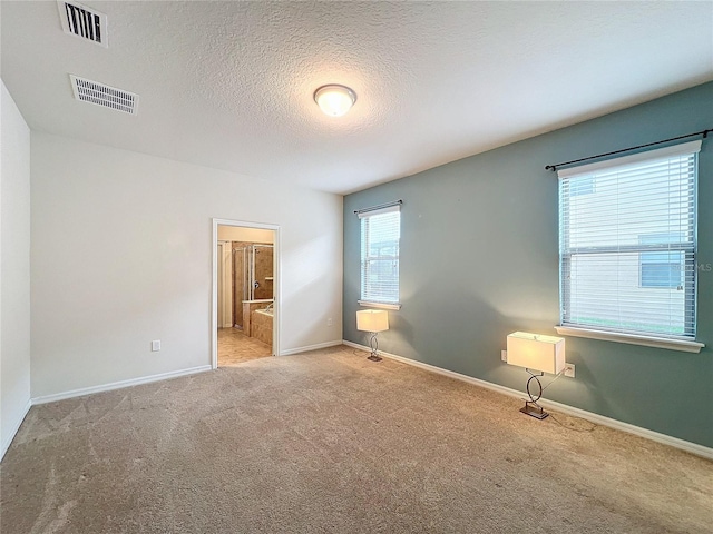 spare room featuring baseboards, visible vents, a textured ceiling, and light colored carpet