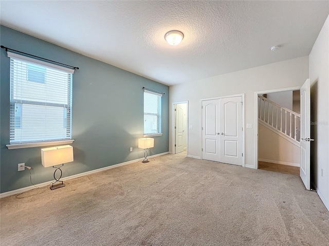 unfurnished bedroom with a textured ceiling, a closet, baseboards, and light colored carpet