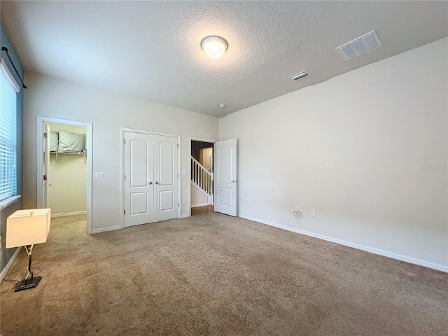 unfurnished bedroom with carpet, visible vents, a textured ceiling, and baseboards