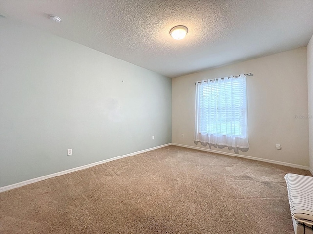 spare room with a textured ceiling, carpet flooring, and baseboards