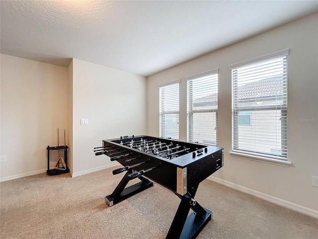 rec room with baseboards, a textured ceiling, and light colored carpet