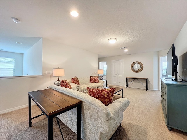 living area with a healthy amount of sunlight, light carpet, a textured ceiling, and baseboards