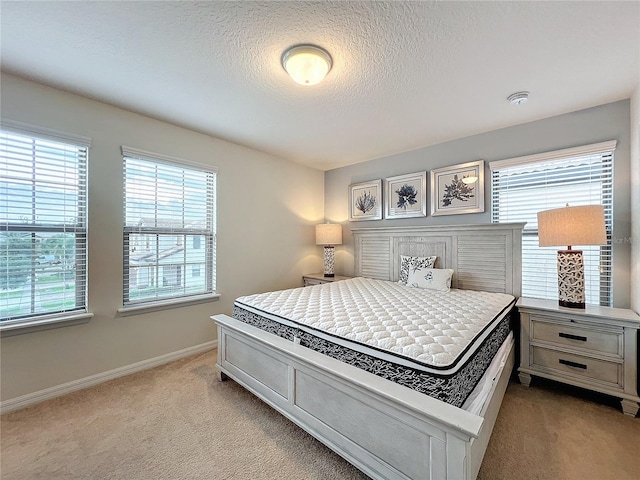 bedroom featuring light colored carpet, a textured ceiling, and baseboards