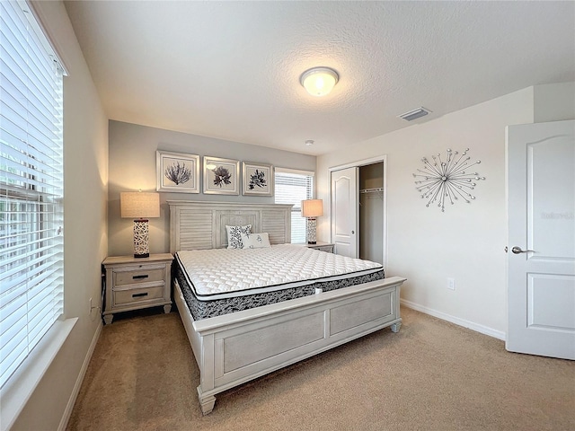 bedroom with baseboards, visible vents, light colored carpet, a textured ceiling, and a closet