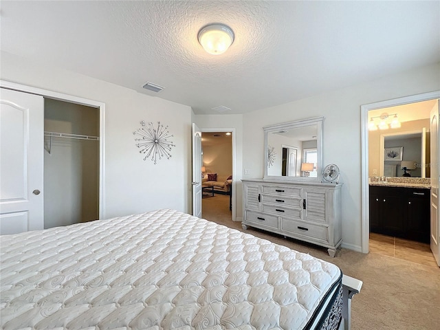 bedroom with a textured ceiling, light carpet, visible vents, a closet, and ensuite bath