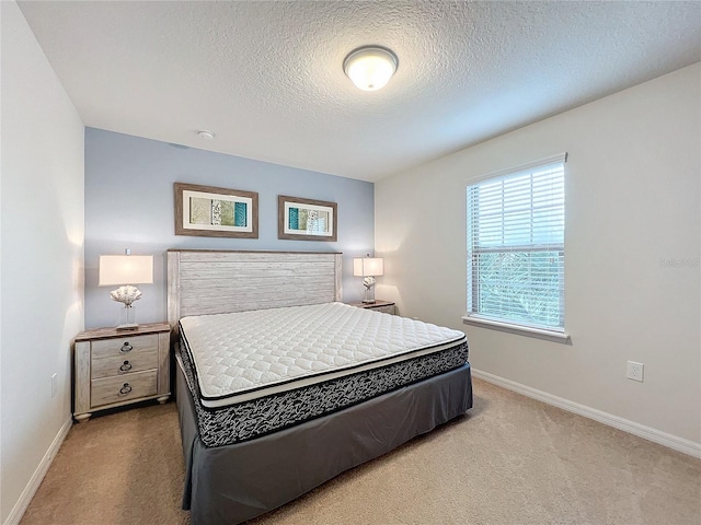 bedroom with baseboards, a textured ceiling, and light colored carpet