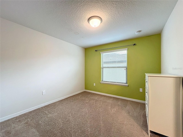 carpeted spare room featuring a textured ceiling and baseboards